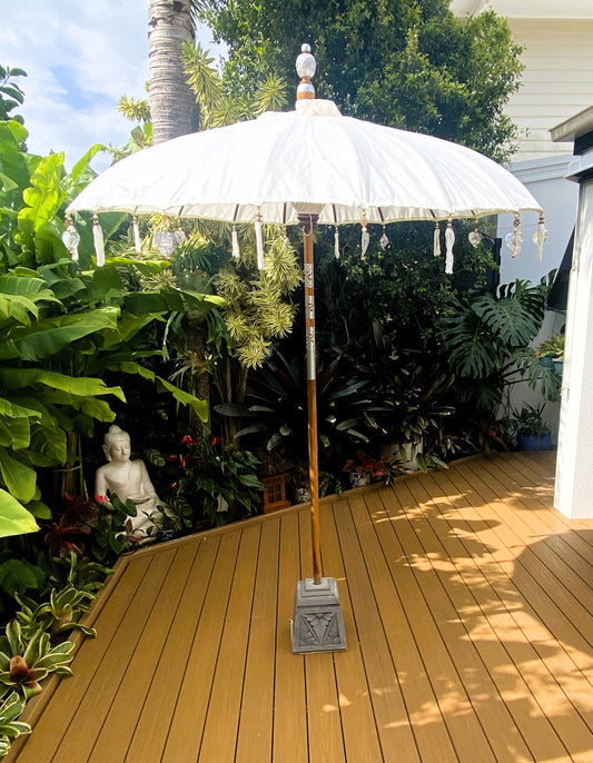 White patio umbrella on a wooden deck with lush greenery in the background