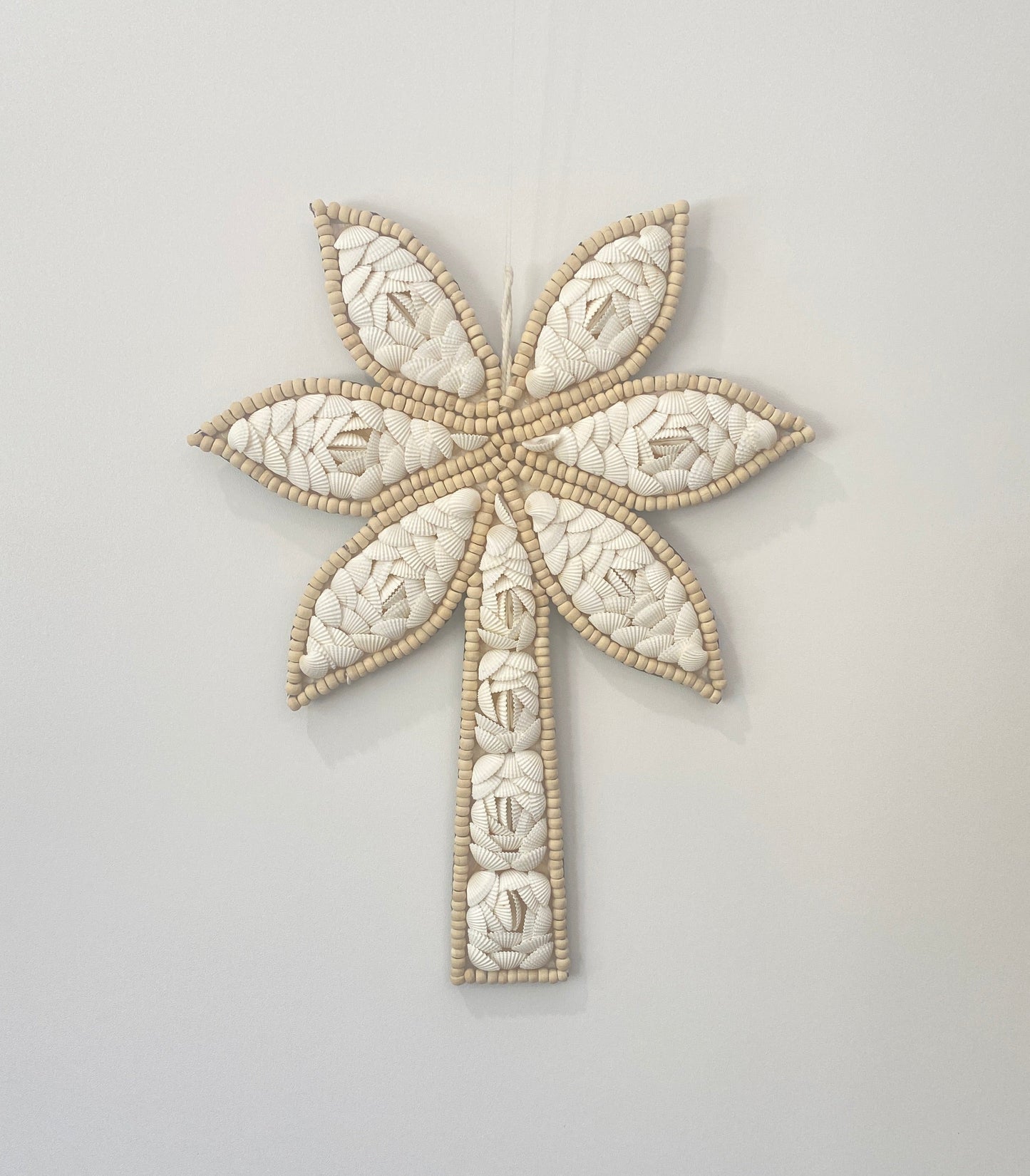 Decorative palm tree wall art with floral shell pattern and wooden beads on a light gray background