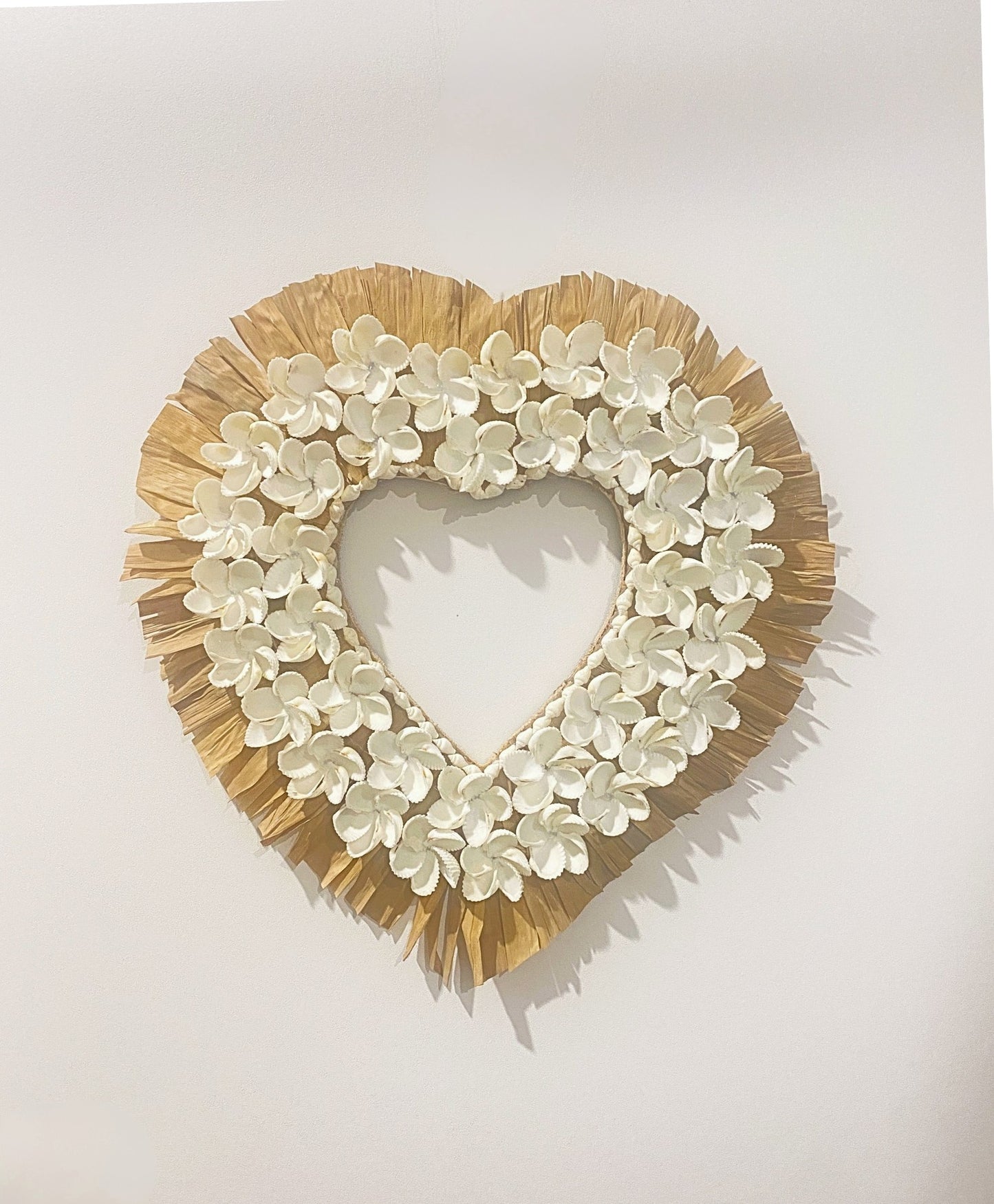 Heart-shaped wreath with white shell flowers and raffia frame on a light background
