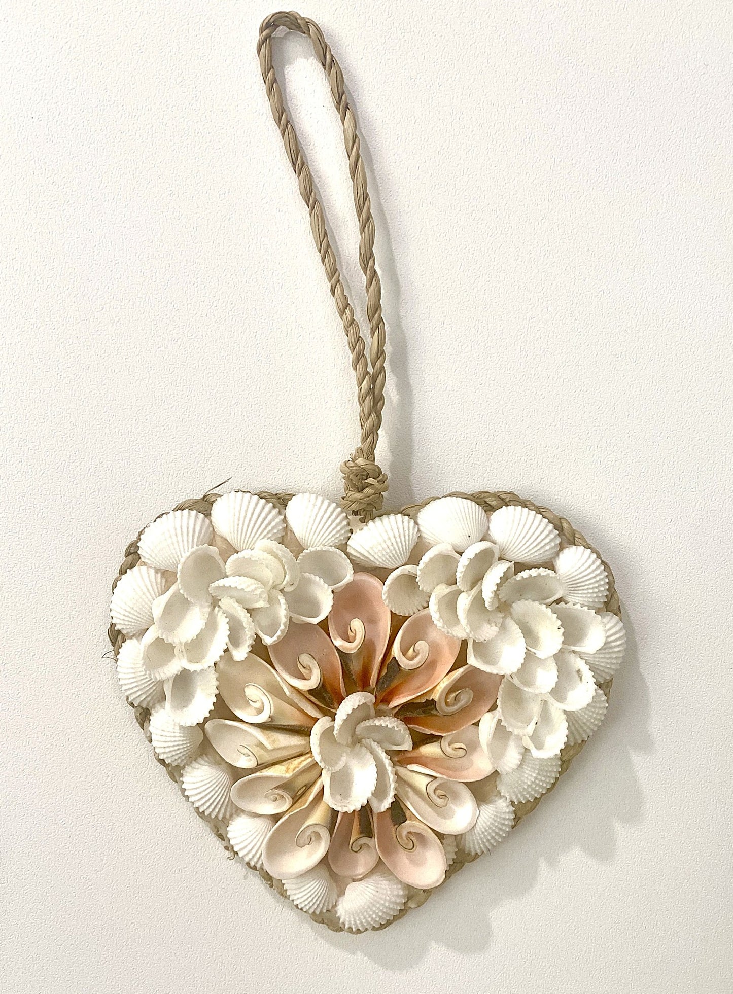 Heart-shaped decorative wall hanging made of seashells with a rope handle on a white background
