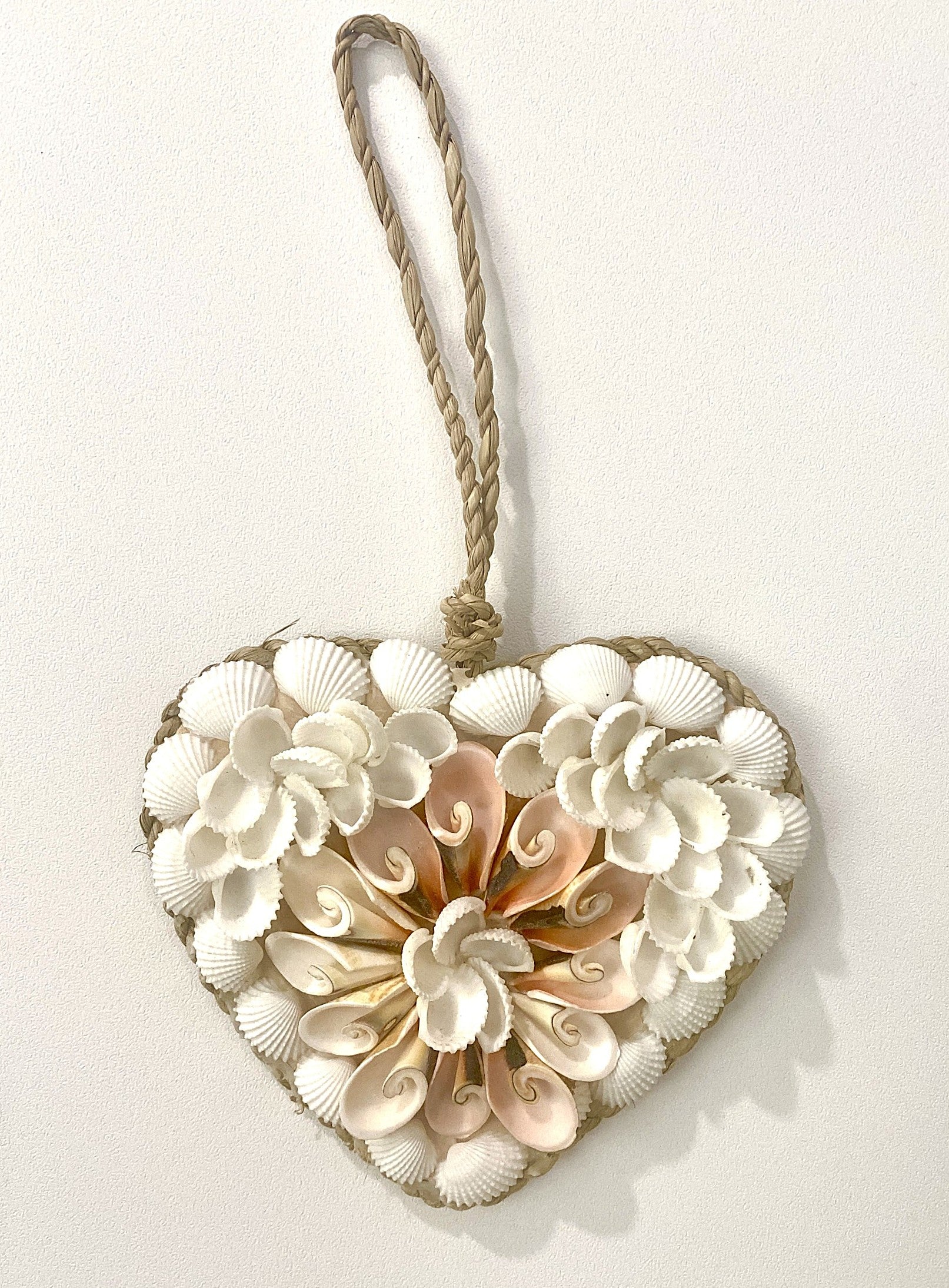 Heart-shaped decorative wall hanging made of seashells with a rope handle on a white background