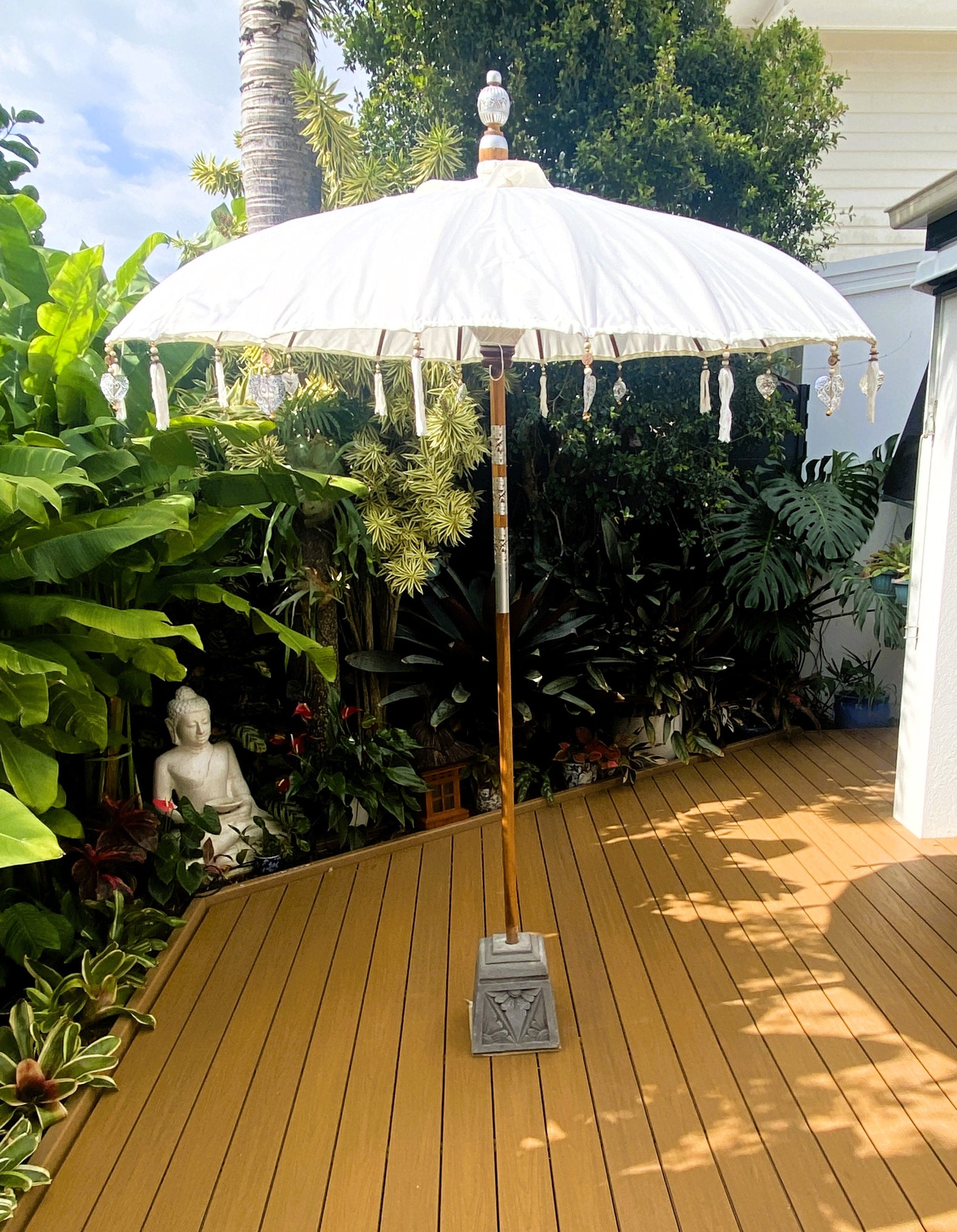 White patio umbrella on a wooden deck with lush greenery in the background