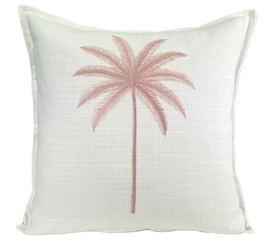 Square white linen cushion cover with a single embroidered pink palm tree centered on the front. The fabric has a subtle woven texture and the palm design features a slender trunk with symmetrical fronds. The cushion measures 50x50cm and is styled in a coastal, tropical theme.
