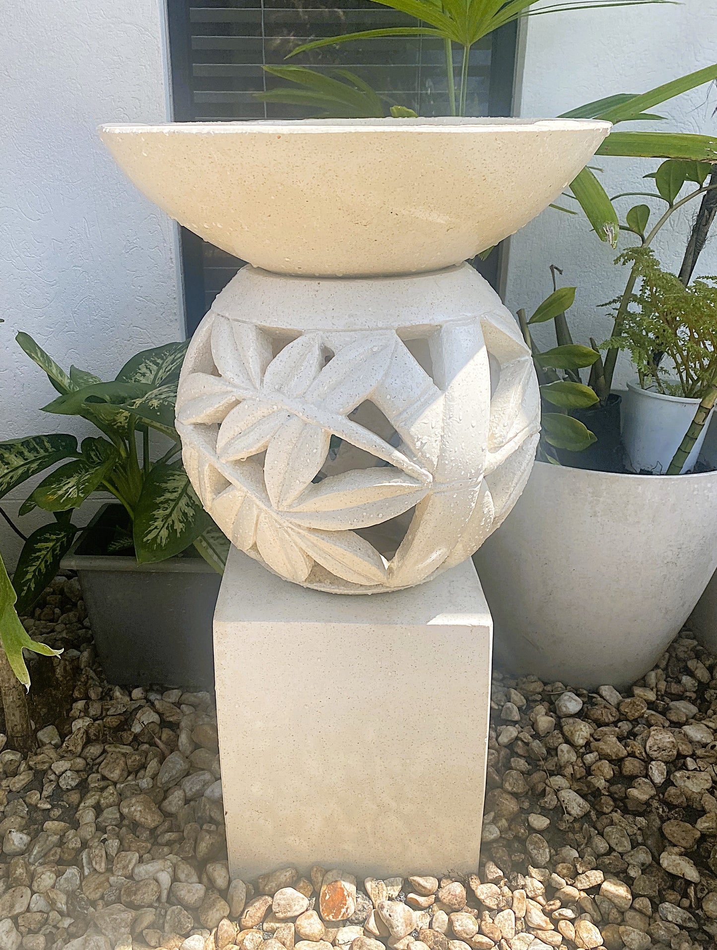 Decorative terrazzo stone lantern and birdbath with bamboo leaf cut out design on a pedestal, surrounded by plants.