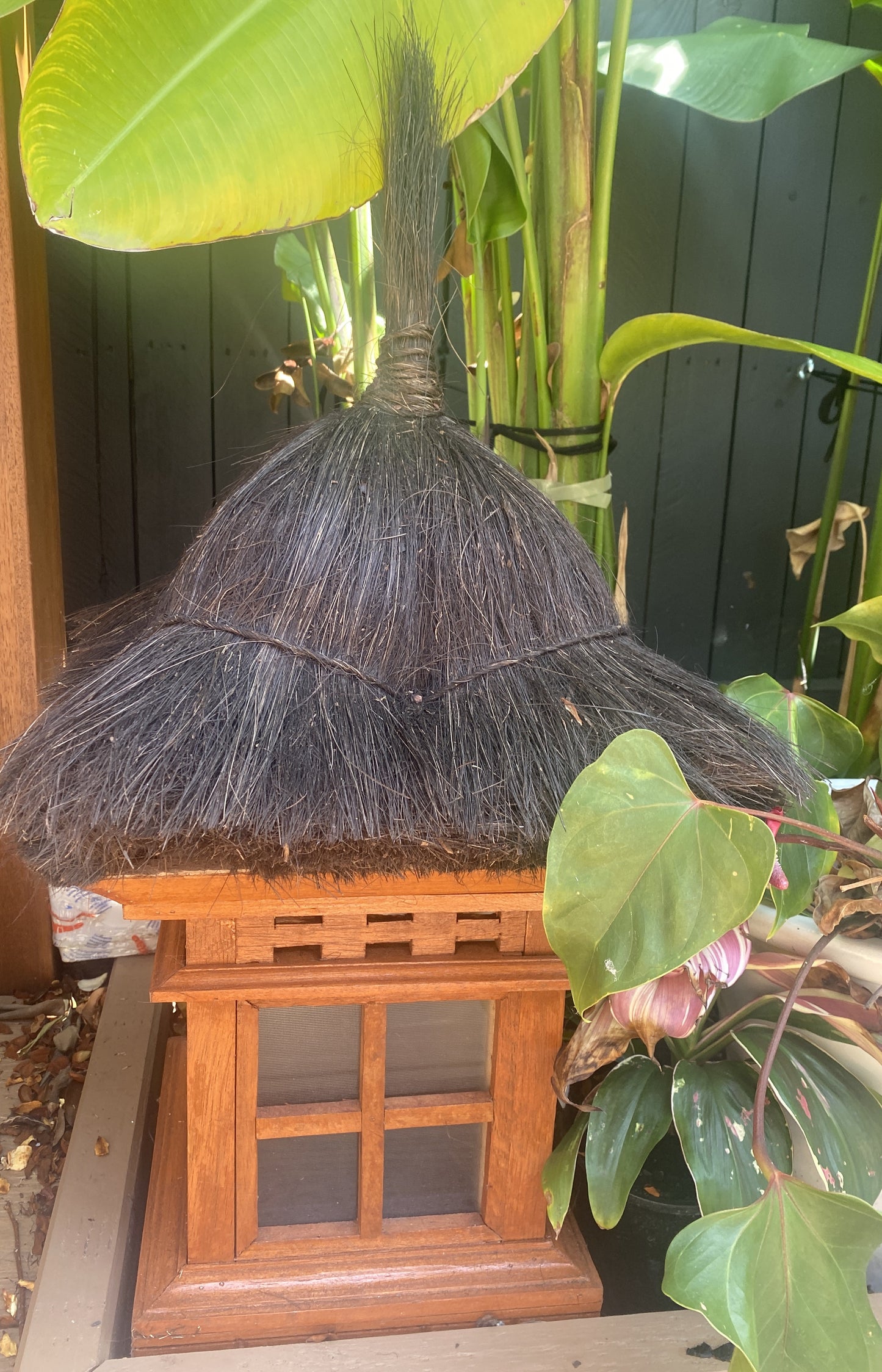 Balinese wooden garden lantern with thatched roof surrounded by green foliage