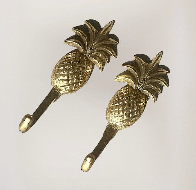 Two gold pineapple-shaped wall hooks on a light gray background