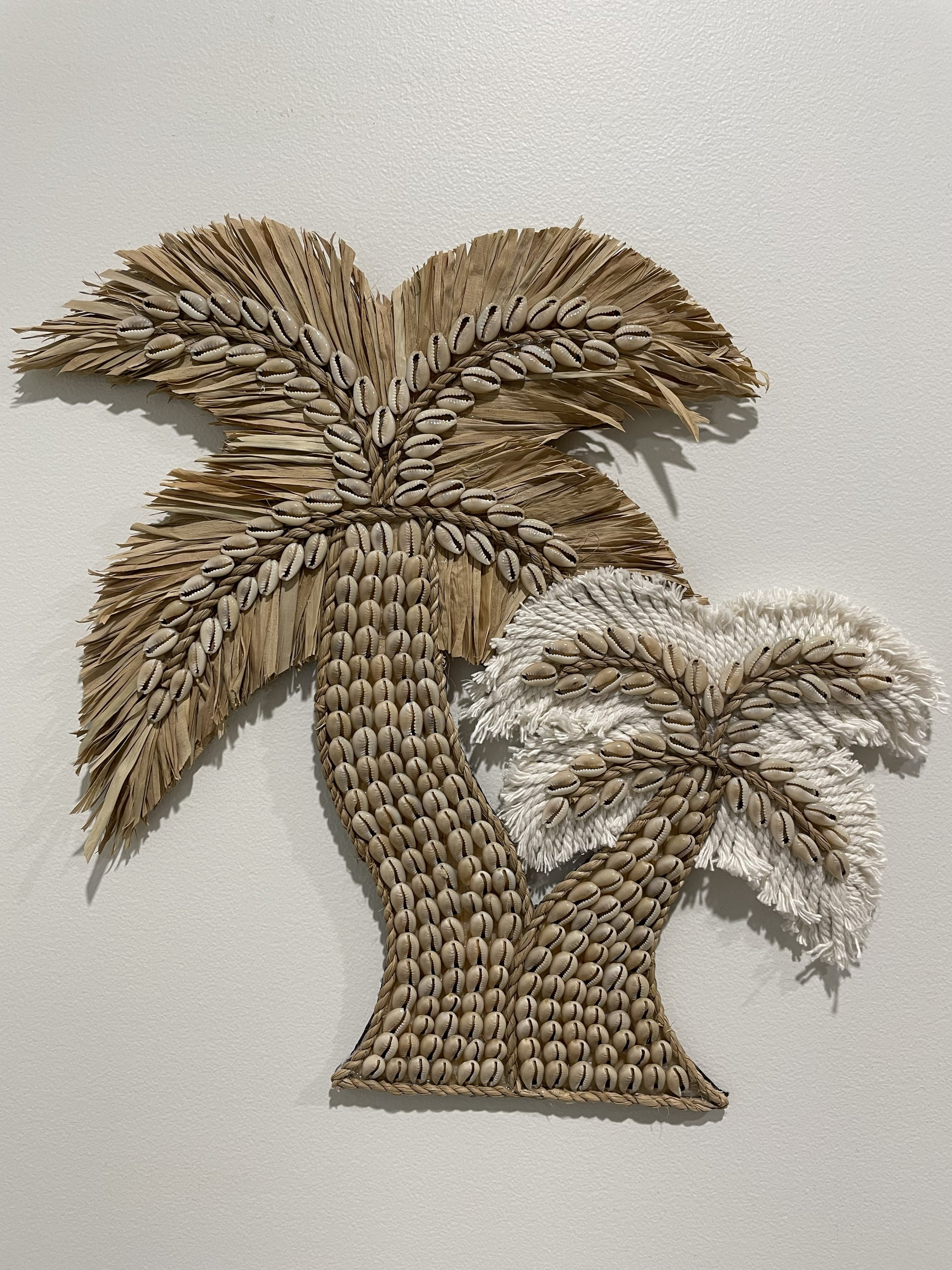 Shell and raffia and cotton twin palm tree design wall art on a plain background
