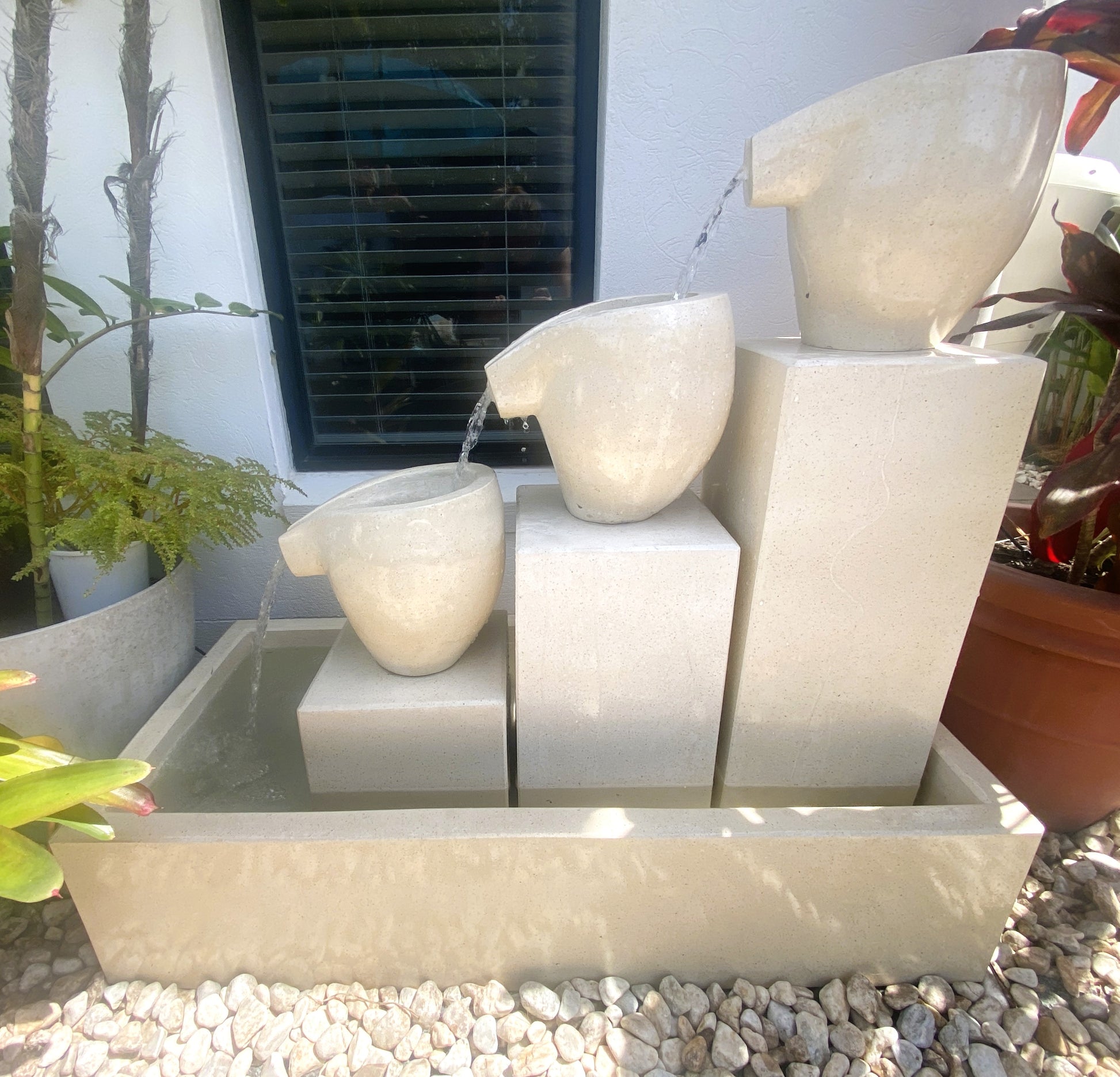 Decorative terrazzo stone water fountain with three bowls in a garden setting.